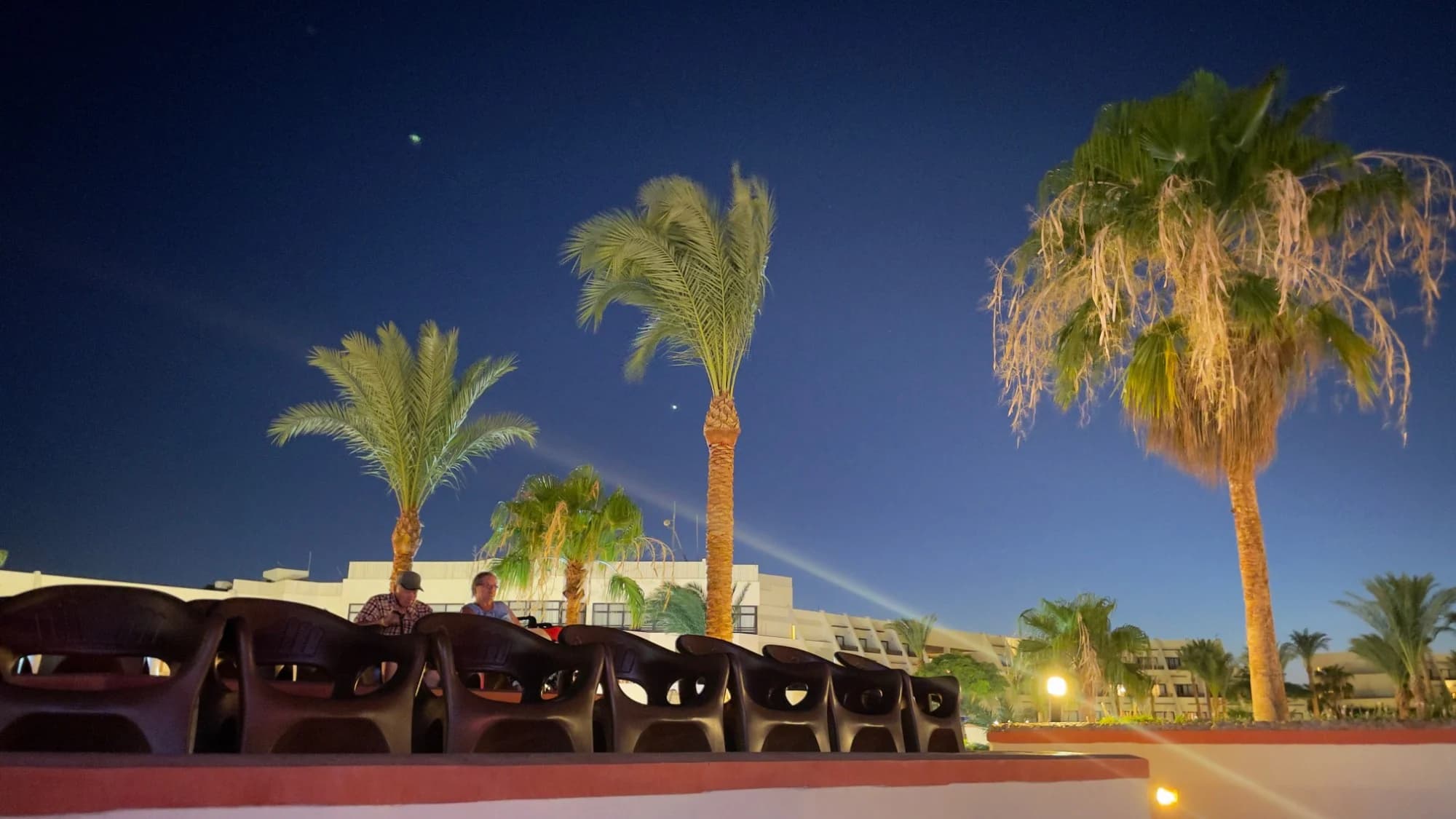 Palmen und Hotelgebäude des Pharaoh Azur Resorts am Abend unter tiefblauem Himmel, im Vordergrund Stuhlreihen auf einer Terrasse